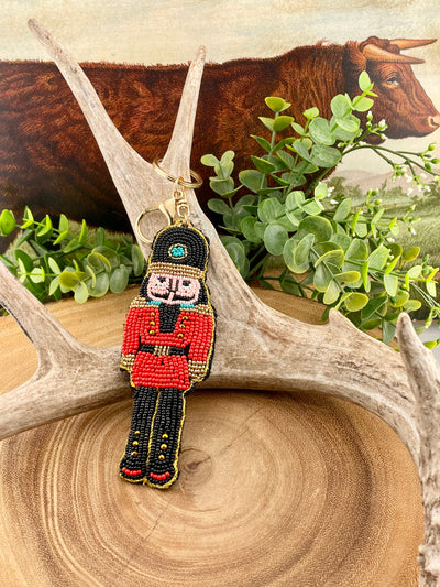 Decorative keychain in the shape of a nutcracker on a wooden surface with greenery and antlers in the background