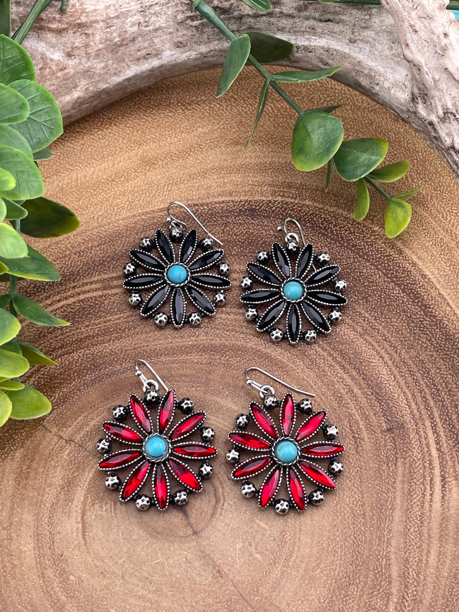 Two sets of floral earrings on a wooden surface with green leaves.