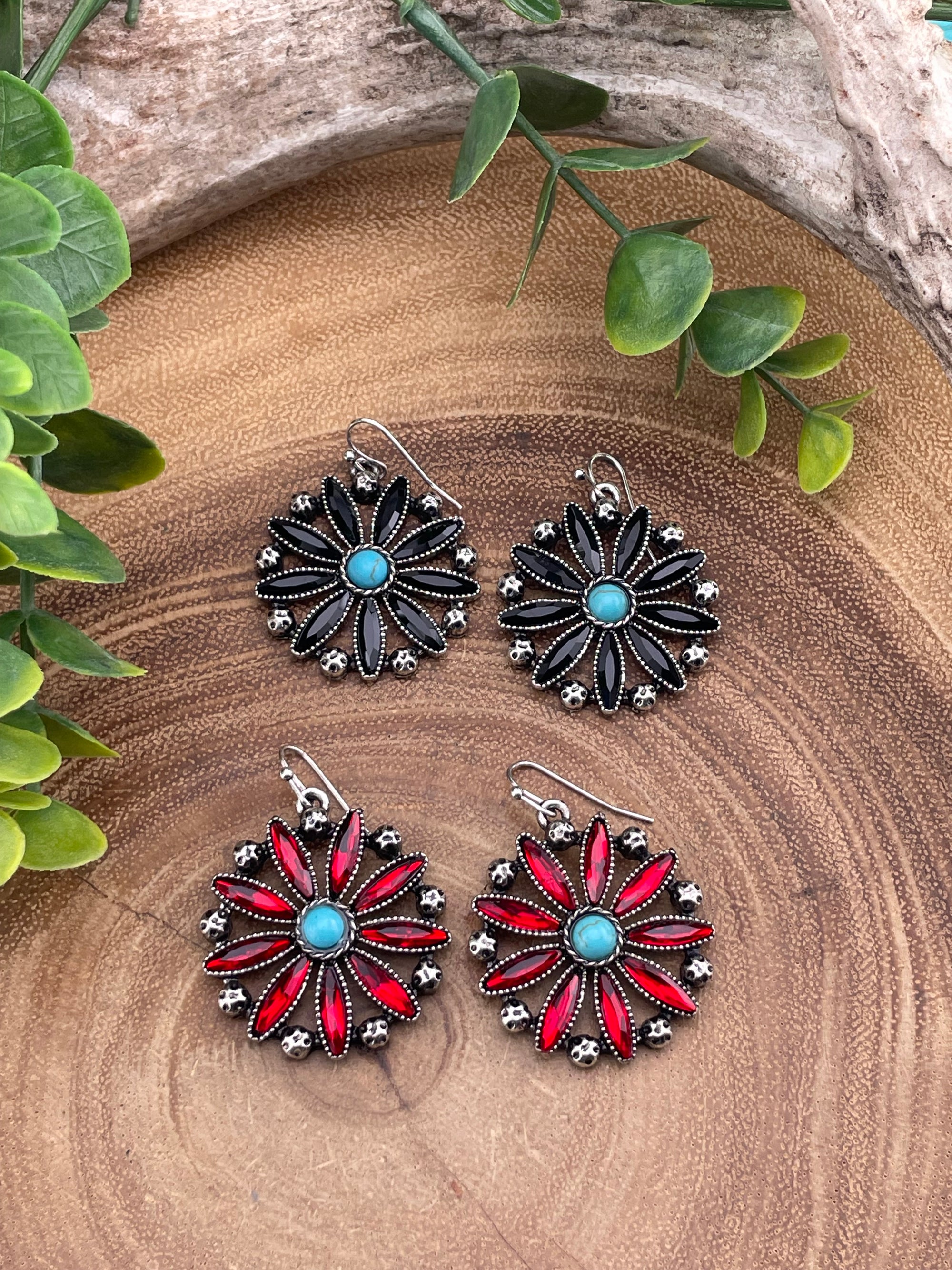 Two sets of floral earrings on a wooden surface with green leaves.