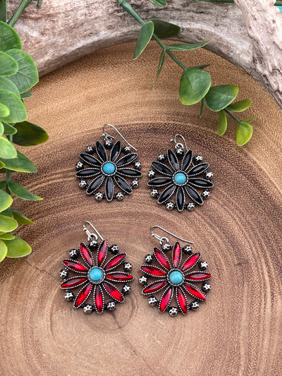 Two sets of floral earrings on a wooden surface with green leaves.