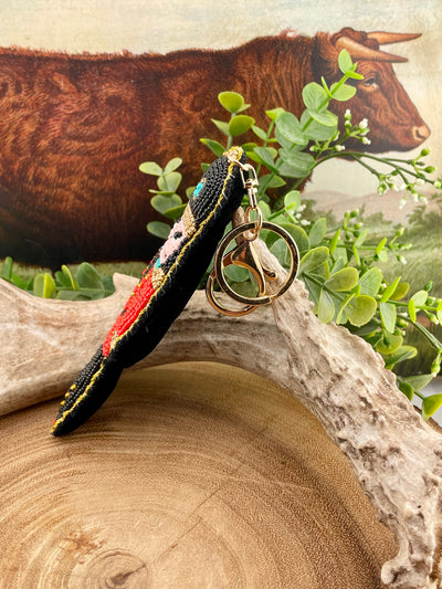 Felt backed beaded keychain on a wooden surface with a cow in the background