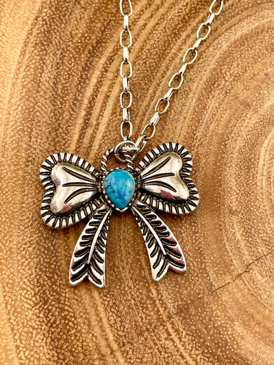 Bow necklace on a wooden surface with a turquoise center stone.