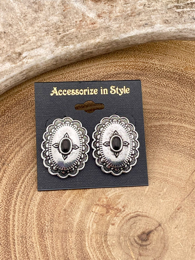 Pair of silver earrings with black center on a 'Accessorize in Style' card, placed on a wooden surface.