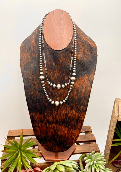 Necklace displayed on a wooden mannequin bust with plants in the background