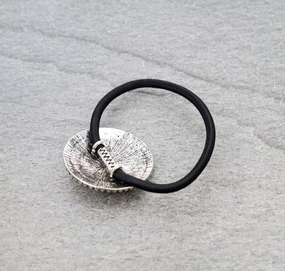 Black hair tie with a silver concho on a gray surface.