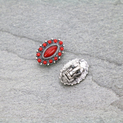 Two decorative buttons, one with red stones and silver border, the other plain silver, on a gray textured surface.