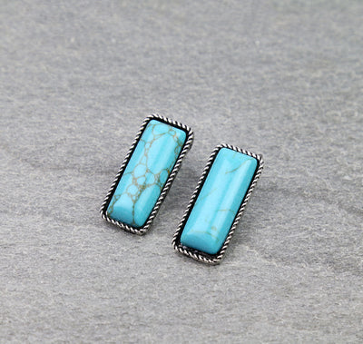 Pair of turquoise earrings with silver frames on a gray background