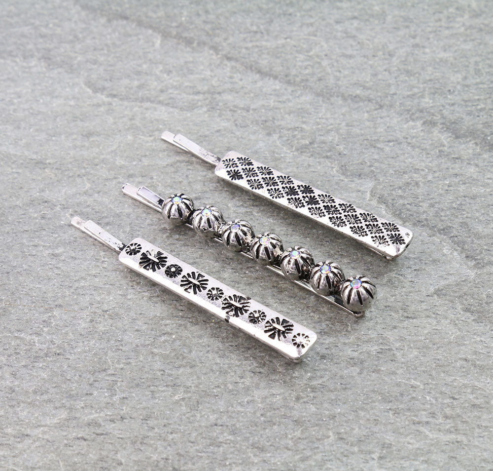 Three silver hair pins with intricate designs on a gray textured background