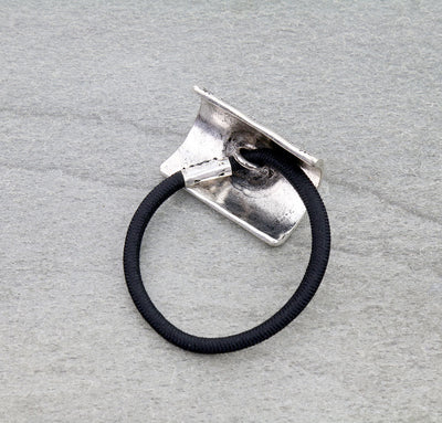 Silver hair tie holder with a black hair tie on a gray background