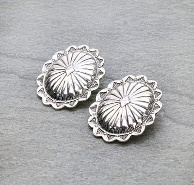Pair of silver concho-style earrings on a gray background
