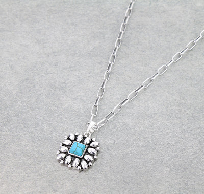 Necklace with a square pendant featuring a turquoise stone on a gray background.