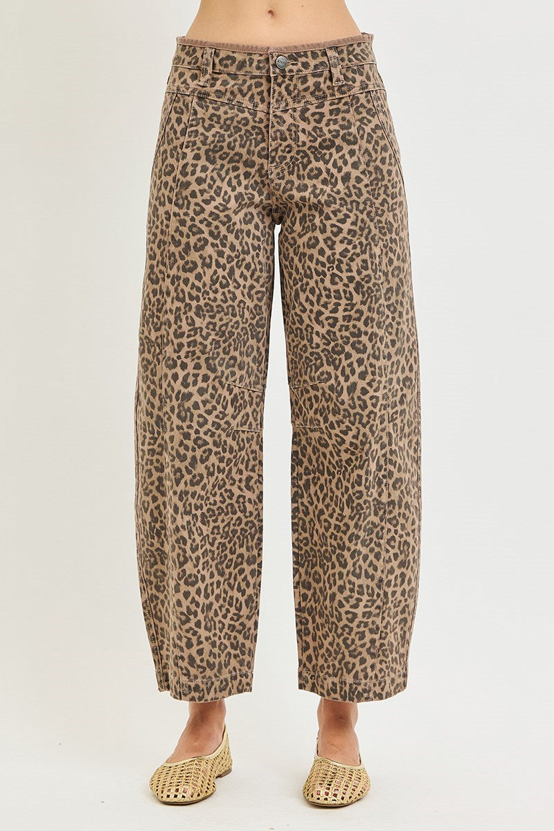 A person wearing leopard-print cropped pants with a tan and brown base and black spots, paired with woven tan flats, shown against a plain light background.