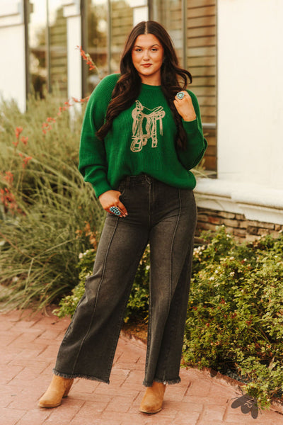 Woman wearing a green sweater with a design, standing outdoors near a building.