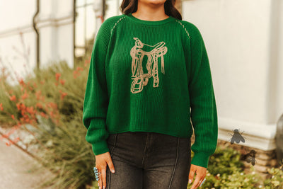 Person wearing a green sweater with a saddle design outdoors.
