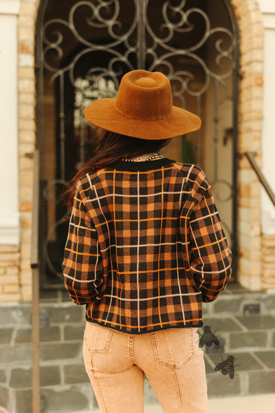 Person wearing a plaid shirt and brown hat standing in front of a decorative door.