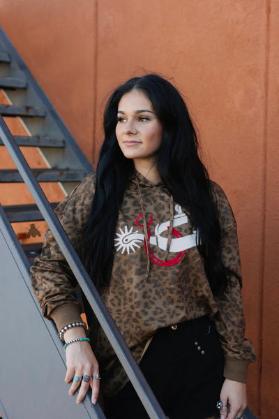Woman wearing a leopard print sweatshirt with a graphic design against an orange wall.