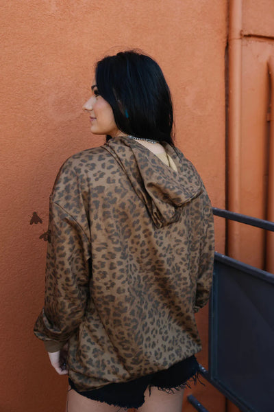 back view of woman wearing leoopard hoodie against an orange wall