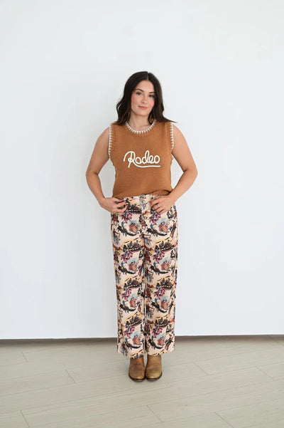 Woman wearing a brown sleeveless top with 'Rodeo' print and floral pants against a white background