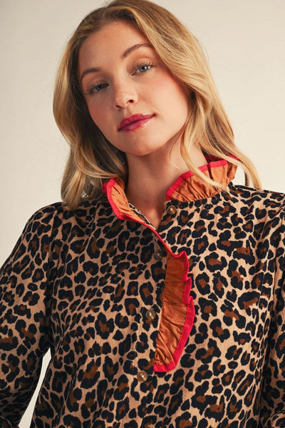 A woman wearing a leopard print blouse with a ruffled orange and red collar, photographed against a plain light beige background.