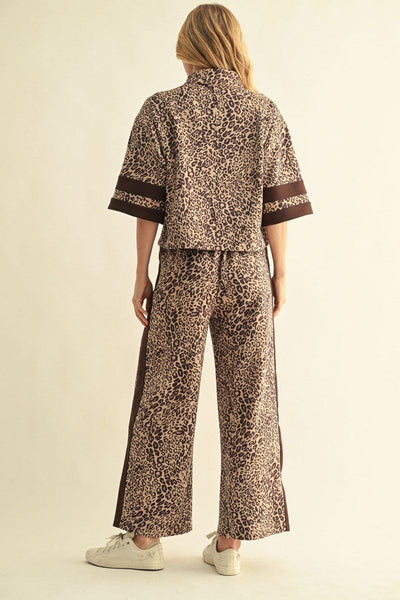A woman modeling a matching two-piece lounge set featuring a brown and beige leopard print pattern with solid brown trim on a light beige studio background. Shown from the back.