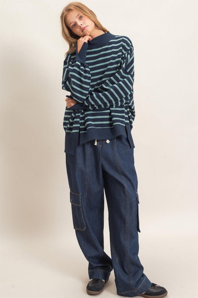 woman wearing a navy/sage striped sweatshirt and jeans with a light background