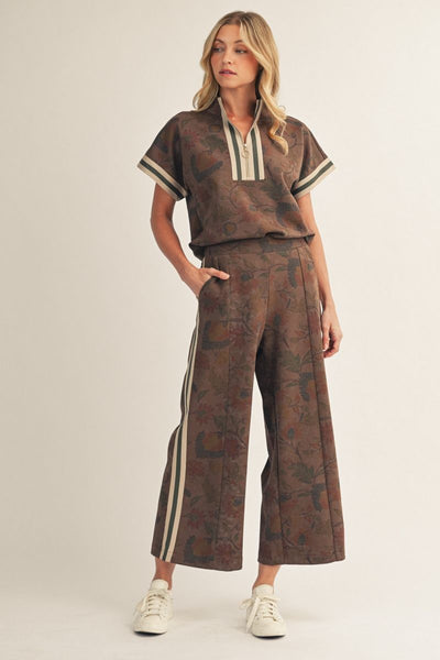 Woman wearing a brown patterned outfit with white accents on a plain background