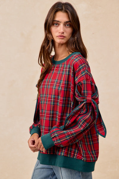 Woman wearing a red plaid sweater with green trim against a beige background