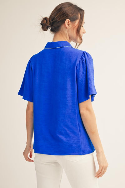 back of model wearing a royal blue v neck blouse with white pants