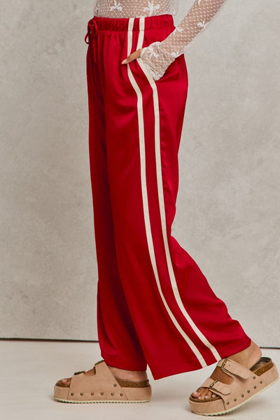 Red pants with white stripes worn by a person on a neutral background