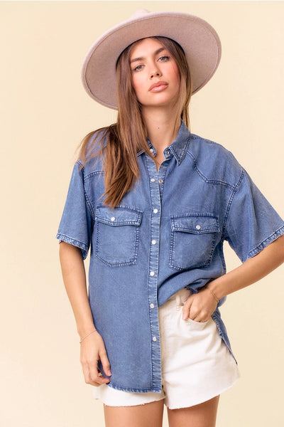 model wearing a hat, short sleeve denim top & white shorts with a tan background