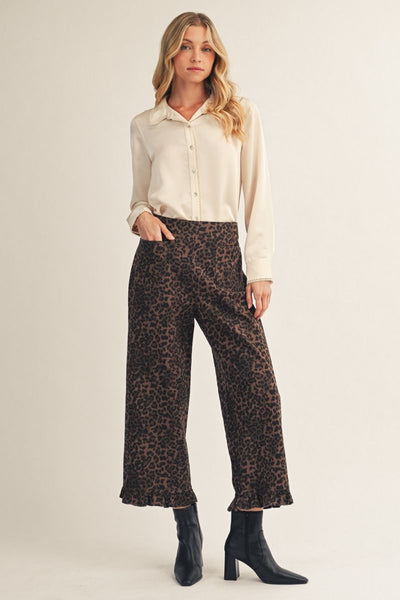 Woman wearing a ivory blouse and leopard print pants on a beige background