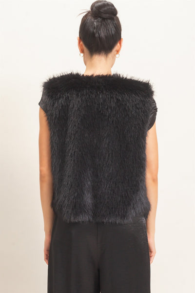 back of model wearing a black satin outfit & black faux fur vest with a light background