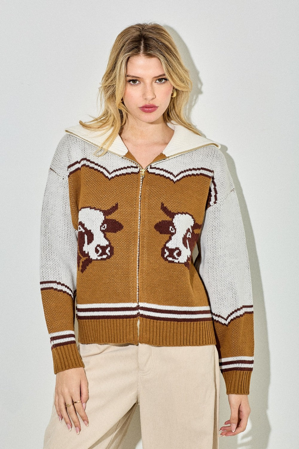 Woman wearing a brown and white sweater with cow designs on a plain background