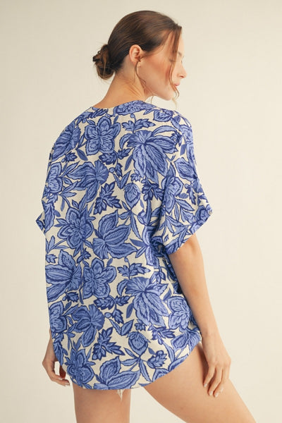 back of model wearing a blue & white floral top with cutoff denim shorts
