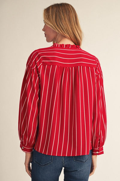 A woman shown from the back wearing a red long-sleeve blouse with thin white vertical stripes and blue jeans, against a plain beige studio background.