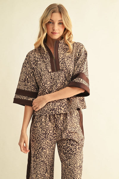A woman modeling a matching two-piece lounge set featuring a brown and beige leopard print pattern with solid brown trim on a light beige studio background.