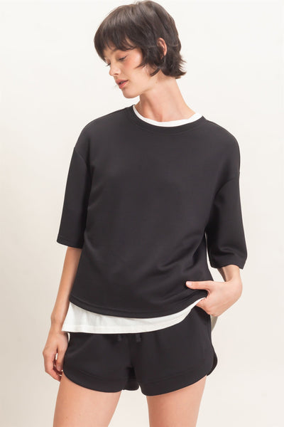 model wearing black short sleeve top with white tshirt underneath and black shorts in front of a light background
