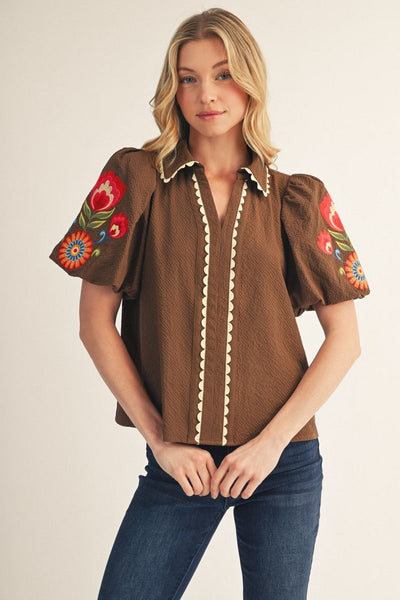 Woman wearing a brown blouse with floral sleeves and blue jeans on a beige background