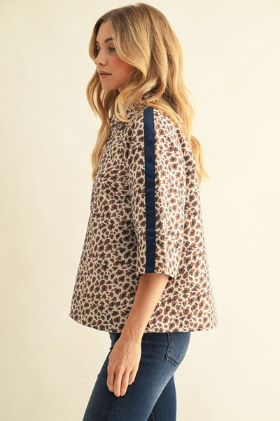 A woman wearing a leopard print blouse with dark navy blue vertical stripes on the sleeves, paired with dark blue jeans, shown from a side profile against a plain cream background.