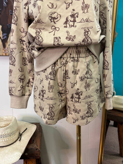 A beige two-piece lounge set with a brown cowboy and cattle print, displayed on a mannequin stand in a boutique setting.