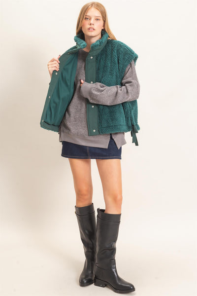 model wearing a gray shirt and jeans skirt with a green Sherpa Vest over it.