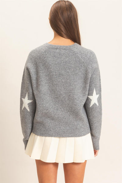 back of model wearing gray sweater with white stars and a white skirt on a light background