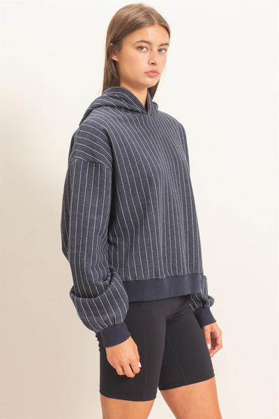 side view of model wearing a navy striped hoodie with black shorts in front of a light background