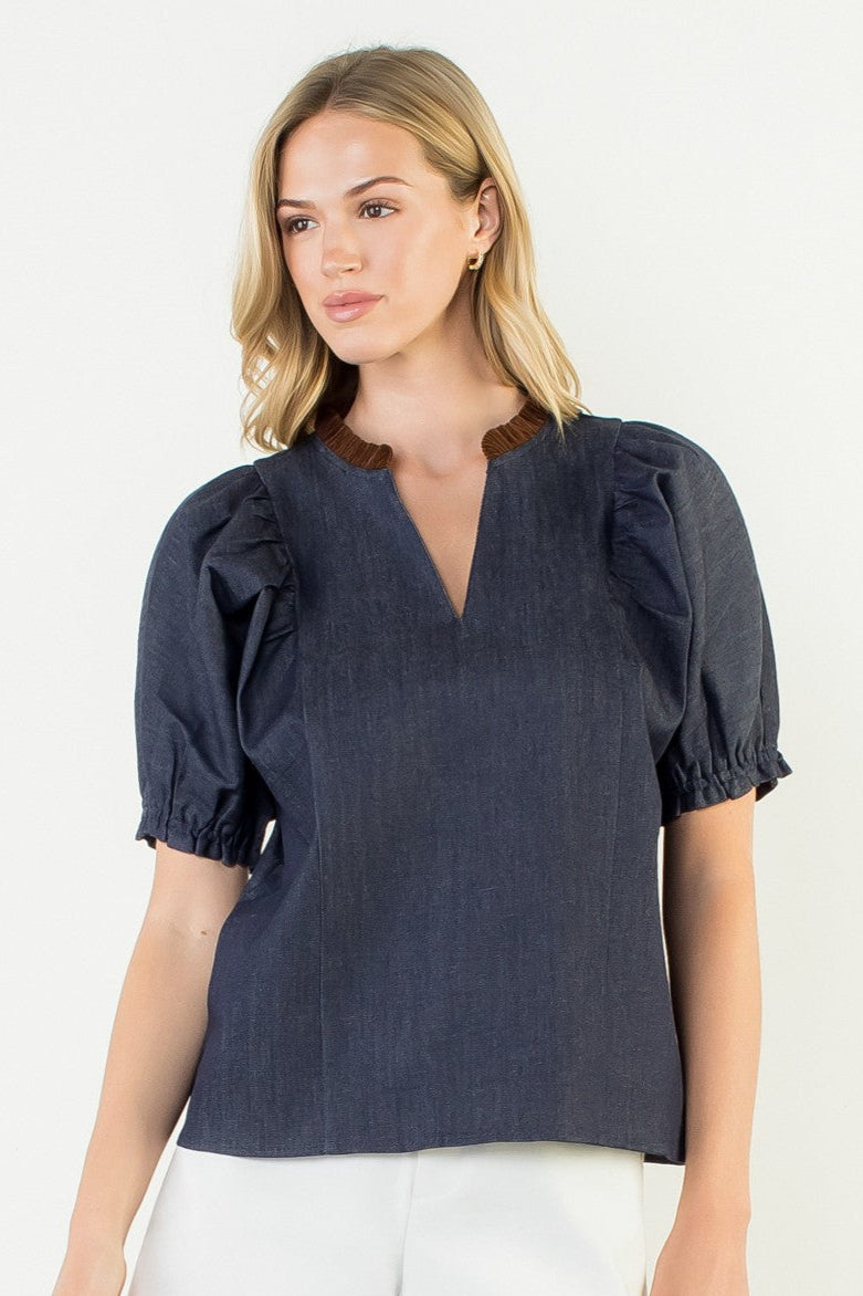 Woman wearing a dark blue blouse with puff sleeves and white shorts on a light background