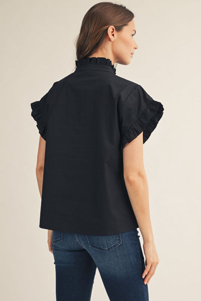 Woman wearing a black blouse with ruffled sleeves on a beige background