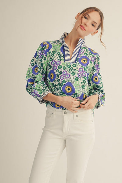 model wearing blue stripe & floral blouse with white pants on a light background