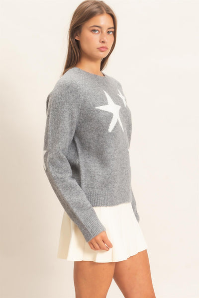 model wearing gray sweater with white stars and a white skirt on a light background shown from the side