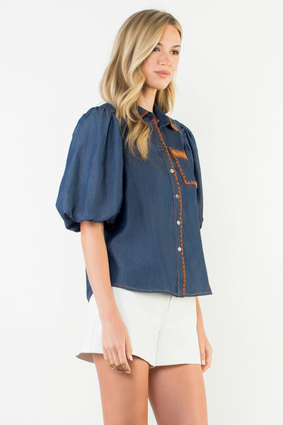 Woman wearing a blue denim shirt with orange stitching on a white background