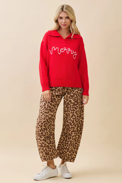 Woman wearing a red sweater with 'Merry' text and leopard print pants on a beige background