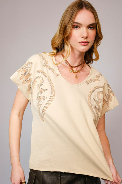 Woman wearing a beige top with intricate designs on a gray background